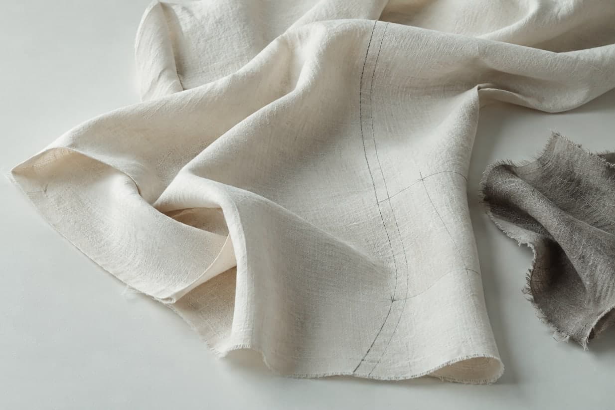 Crumpled ecru linen marked with construction lines, beside a piece of grey linen