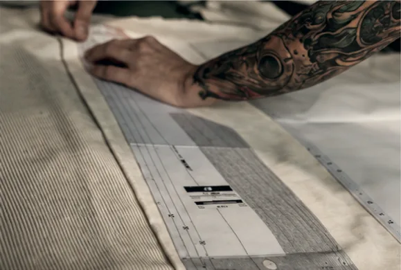 Un bras tatoué trace un patron à la règle