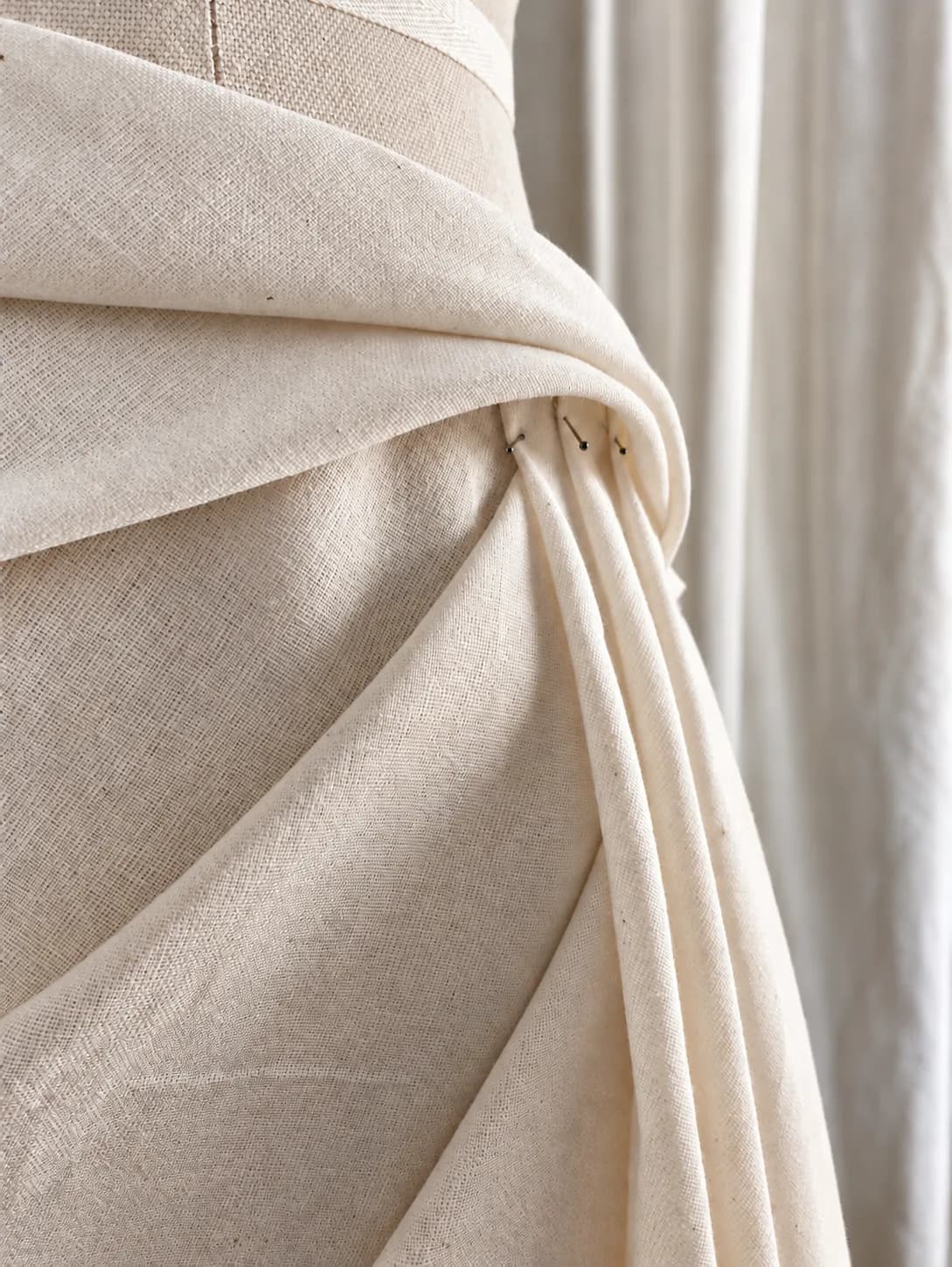 A drape of unbleached calico pinned on a dress form