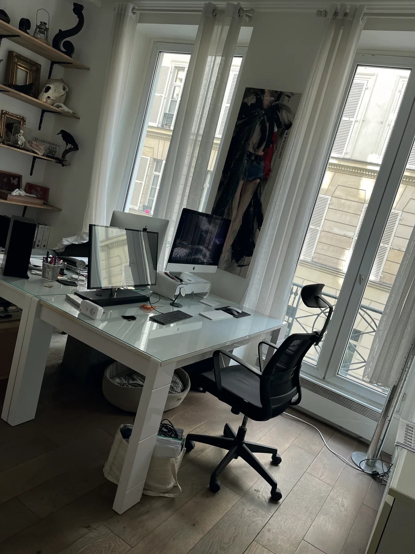 The studio office: two screens on a white desk, tall windows onto the street