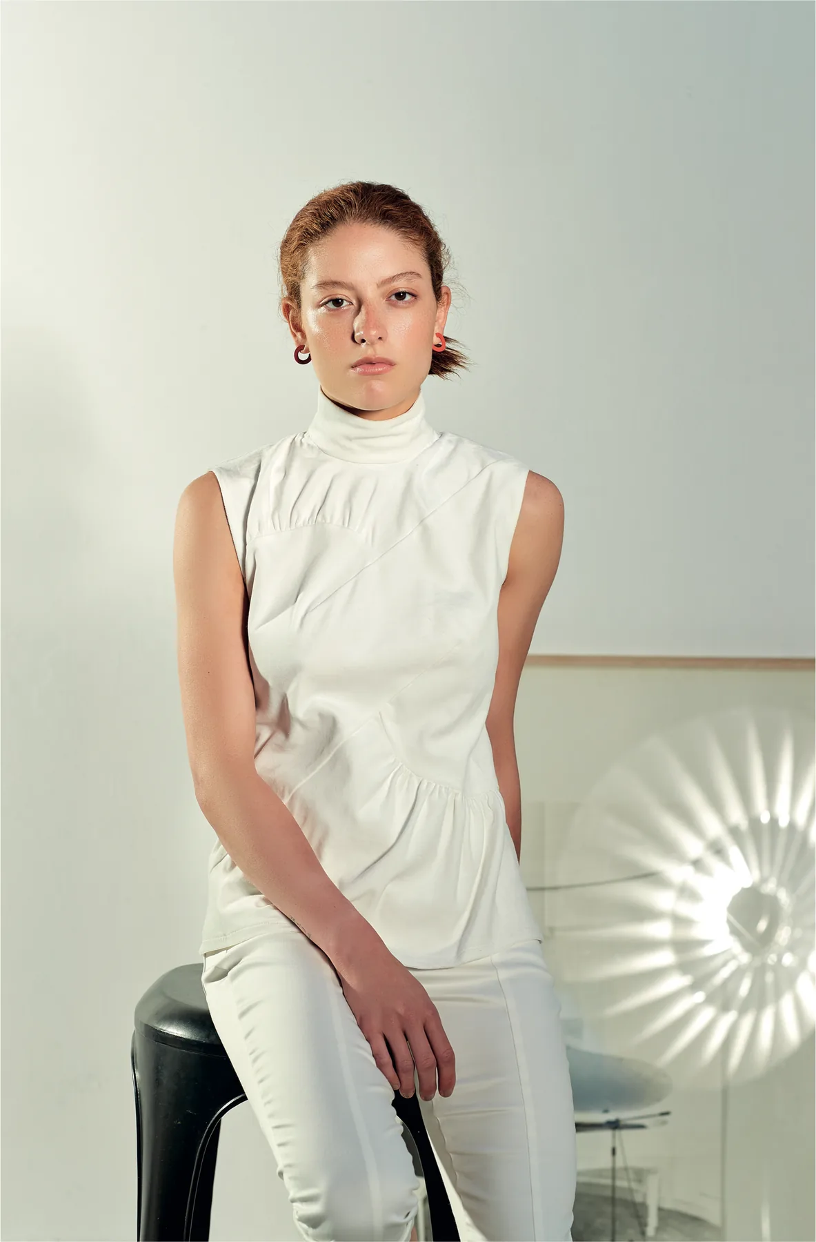 The finished garment: a young woman seated, in a sleeveless high-necked white top and white trousers