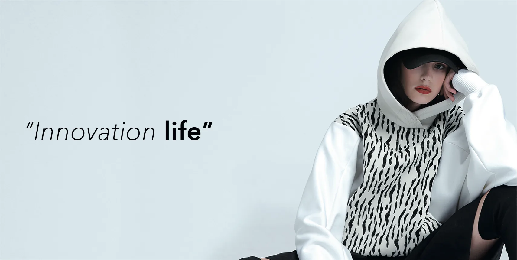 “Innovation life”: a model sitting in a white hoodie with a black-and-white zebra front and a black cap, against a pale blue background