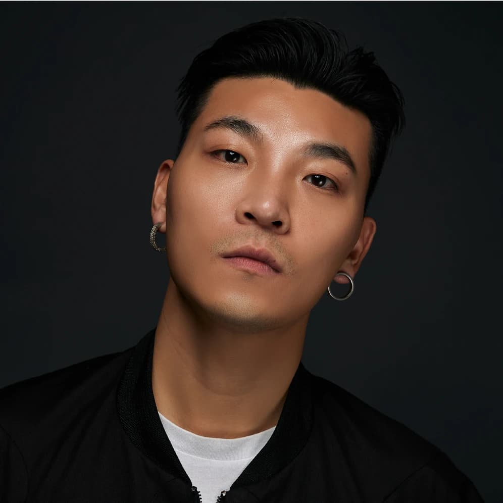 Portrait of Shibo Li: black hair swept back, hoop earrings and a black jacket, against a dark background