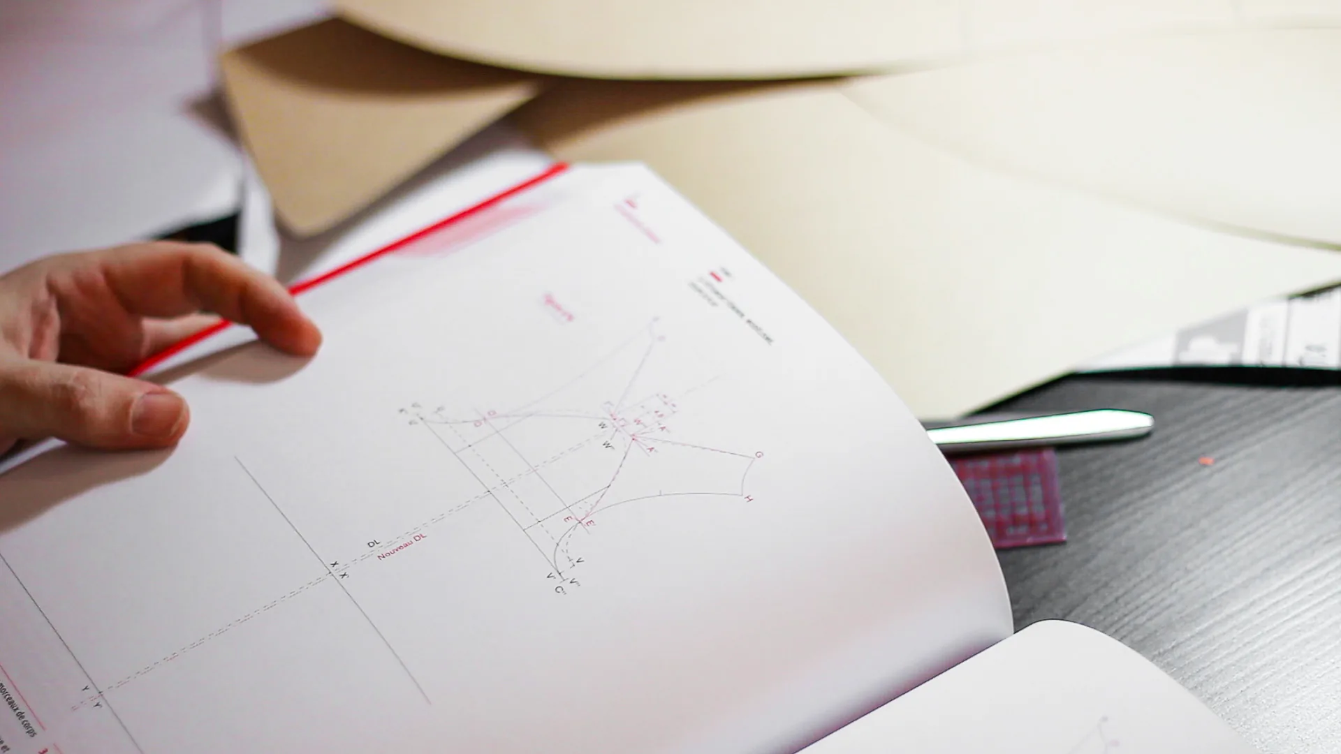 A hand holding a patternmaking book open at a pattern draft